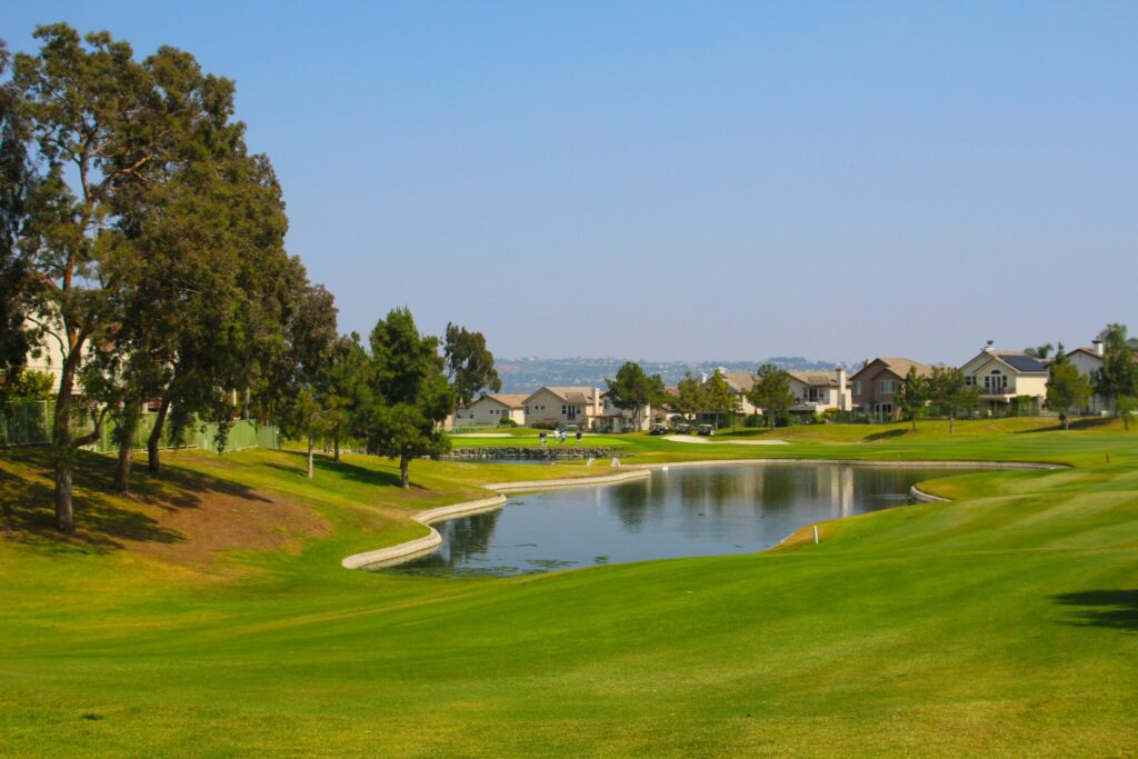 a golf course with green leafed tree and a pond in the middle
